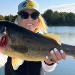 Woman proudly holding a large fish by the water.