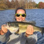 Person holding a large fish by a lake, smiling.