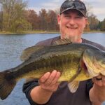 Man proudly holding a large fish by a lake.