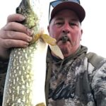Man holding a large fish with a cigar in his mouth.