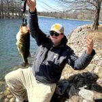 Man proudly holding a large fish by a lakeside.