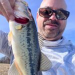 Man holding a largemouth bass, smiling in sunglasses.