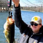 Man proudly holding a large fish by the water.