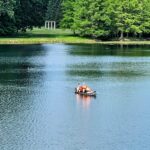 People relaxing on a small boat in a tranquil lake surrounded by greenery.