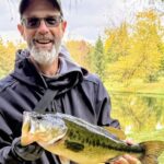 Man proudly holding a large fish by a scenic lake.