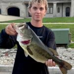 Young man proudly holding a large bass fish he caught.