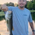 A man proudly holding a large fish he caught by the water.