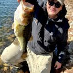 Person proudly holding a large fish by the water.