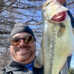 Man smiling and holding a large fish outdoors.
