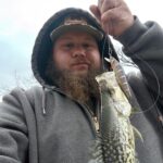 Man proudly holding a freshly caught fish outdoors.