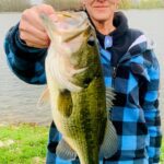 Person holding a large bass fish by the lake.
