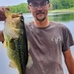 Man proudly holding a large fish by a lake.