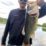 Man proudly holding a large fish he caught by the lake.