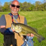 Man proudly holding a large fish in a sunny outdoor setting.