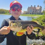 A young man holding a large bass fish in front of a castle.